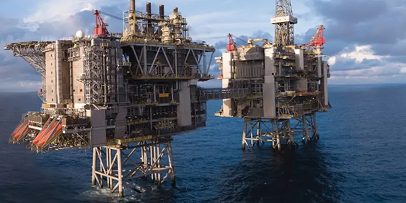 Two large offshore oil rigs stand in a vast, blue ocean under a partly cloudy sky