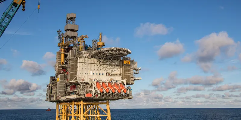 Offshore oil platform with industrial structures and cranes, set against a clear blue sky and ocean.